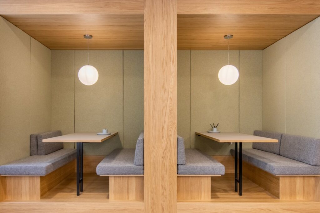 Twee moderne houten zithoeken met grijze kussens en hanglampen in een kantoorruimte aan de Coolsingel 65.