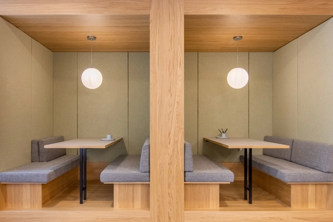 Twee moderne houten zithoeken met grijze kussens en hanglampen in een kantoorruimte aan de Coolsingel 65.