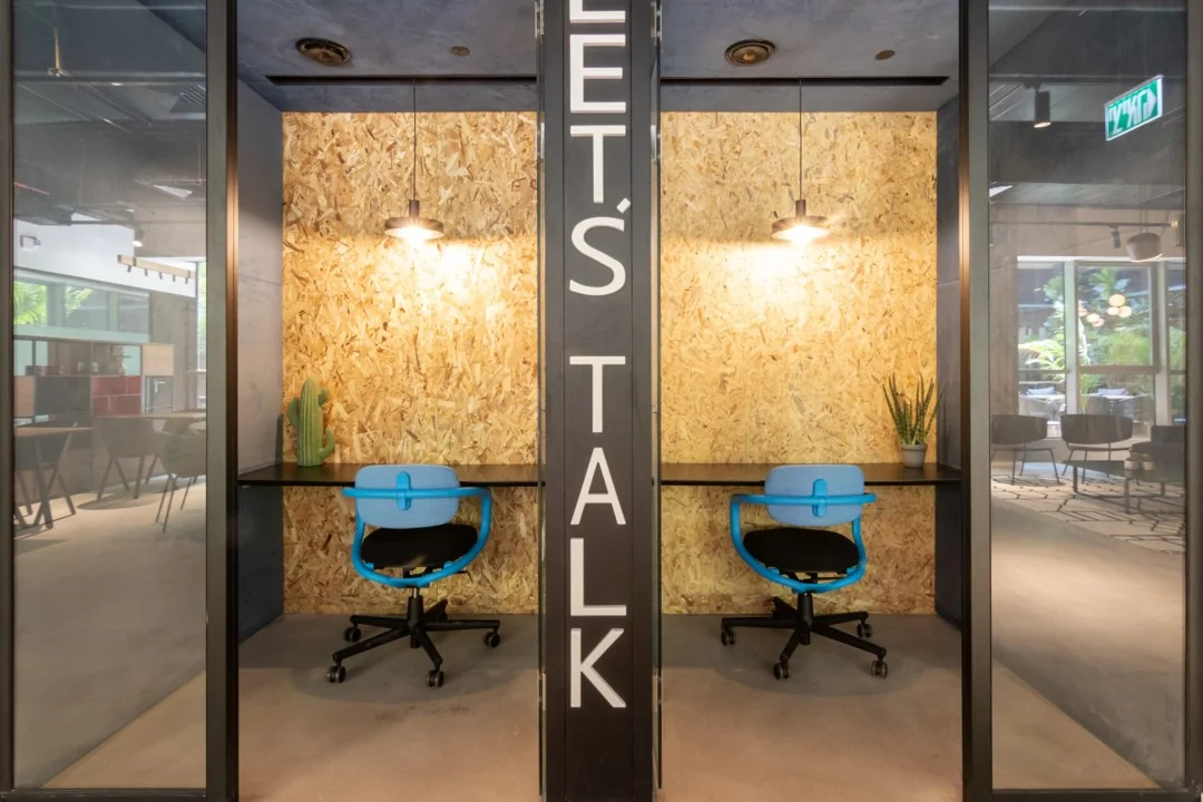 Twee moderne bel- of werkruimtes in Coolsingel 65 met houten wanden, blauwe bureaustoelen en de tekst "LET'S TALK" ertussen.