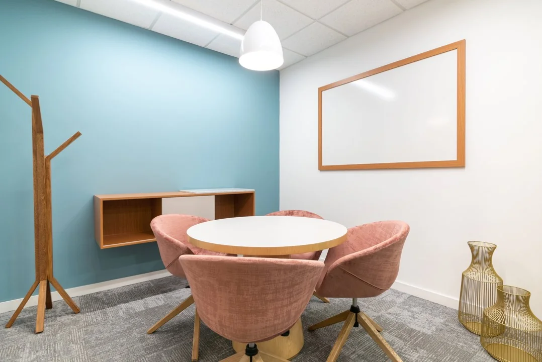 Kleine vergaderruimte met een ronde tafel, vier roze stoelen, een blauw-witte wand en houten accenten in Coolsingel 65.