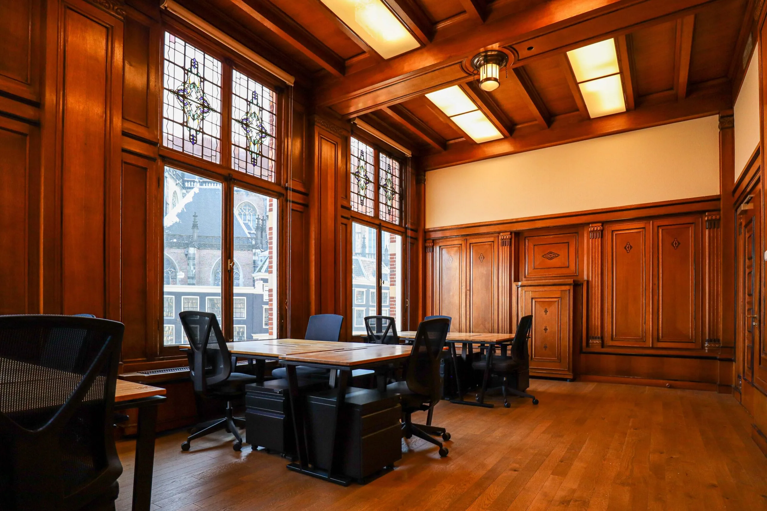 Klassiek ingerichte vergaderruimte DAM 2 met houten lambrisering, glas-in-loodramen en moderne bureaustoelen.