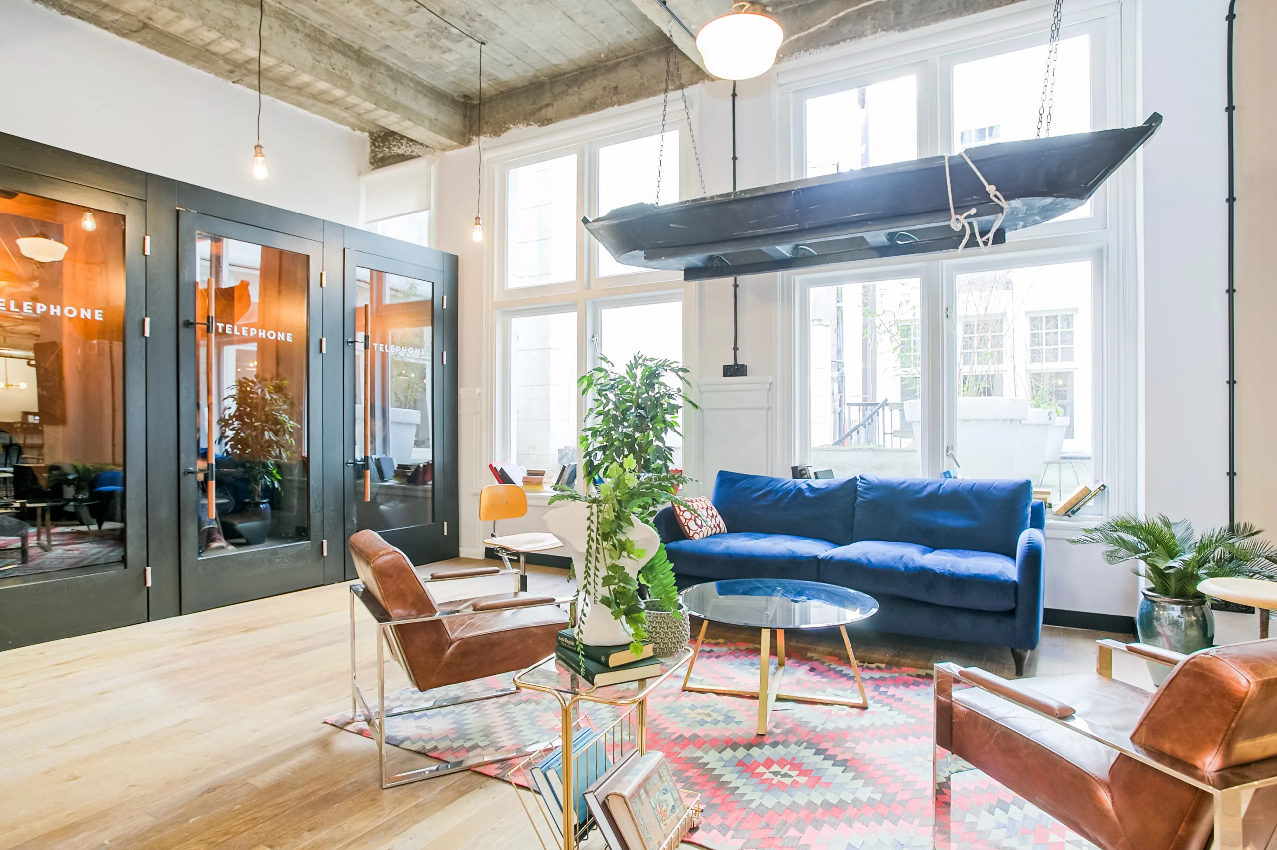 Stijlvol ingerichte lounge met blauw bankstel, hangende boot en glazen belcabines in werkruimte DAM 3.