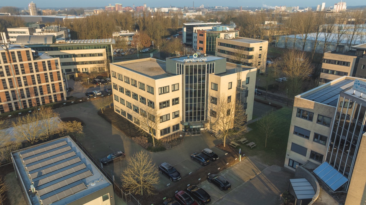 Luchtfoto van het kantoorgebouw van CIMsolutions op bedrijventerrein, omringd door andere kantoren en parkeerplaatsen.