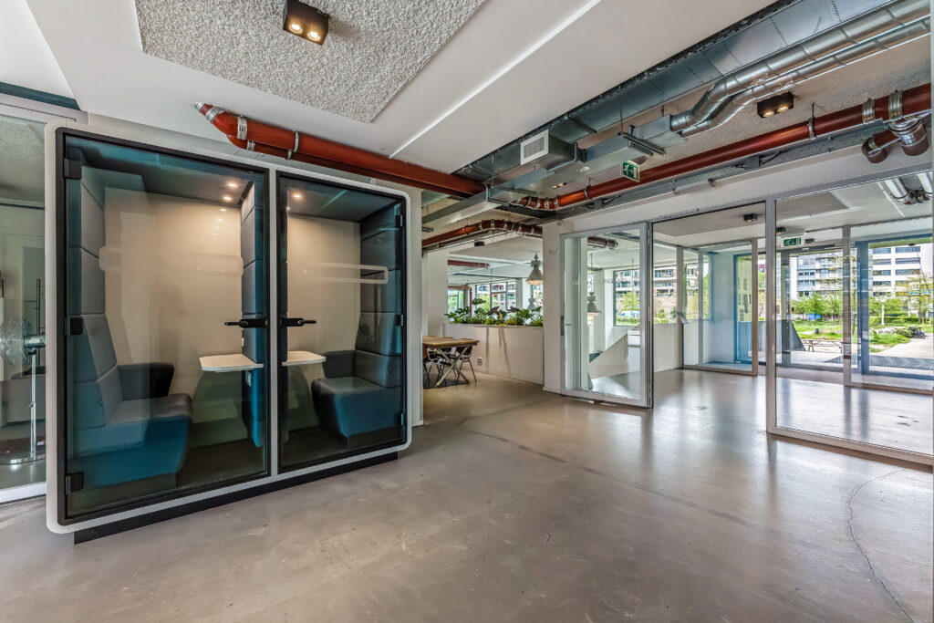 Moderne kantoorruimte met twee afgesloten akoestische belcabines en glazen wanden die uitzicht bieden op een groene buitenomgeving.