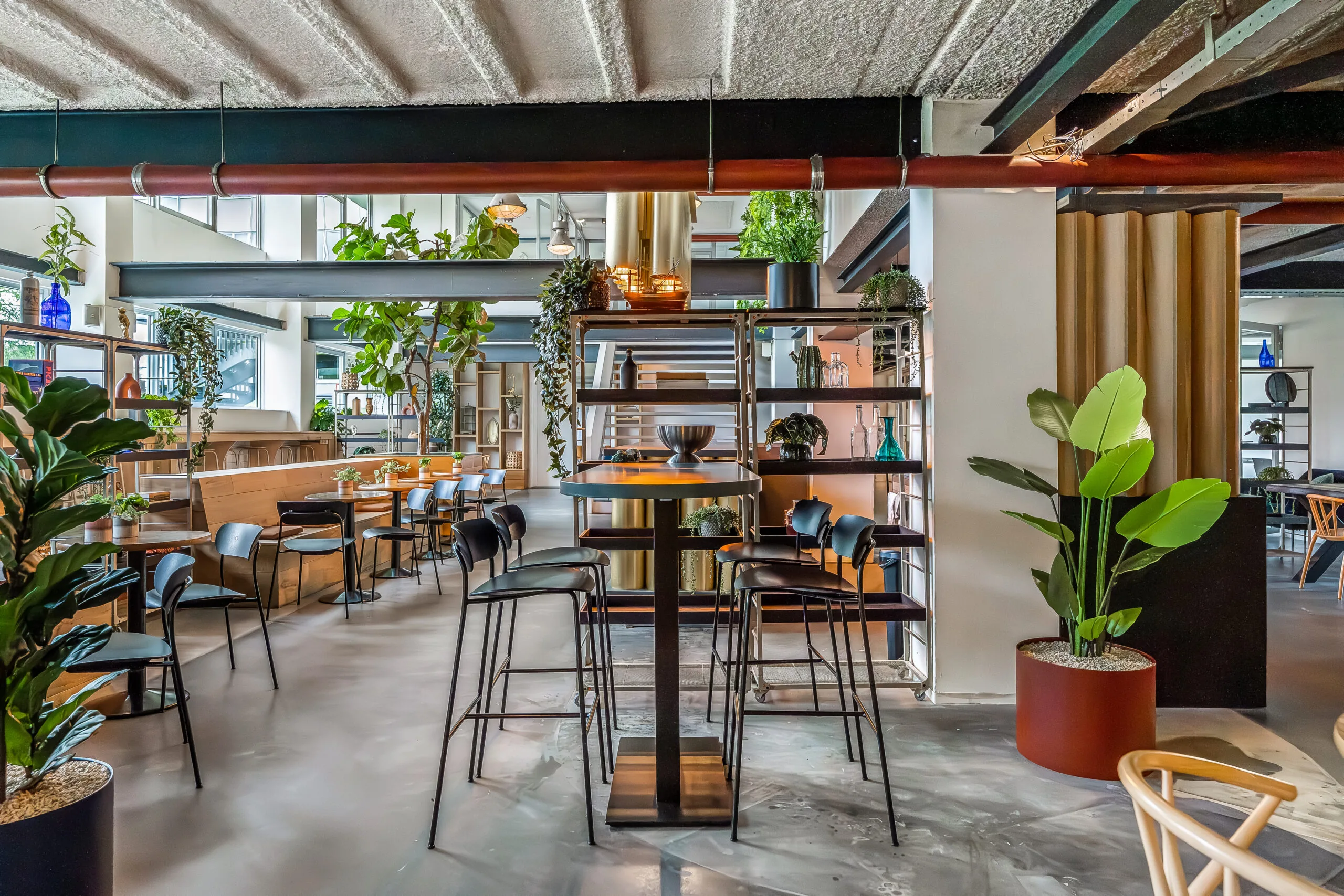 Modern ingericht restaurant met veel groen, houten accenten en industriële details.