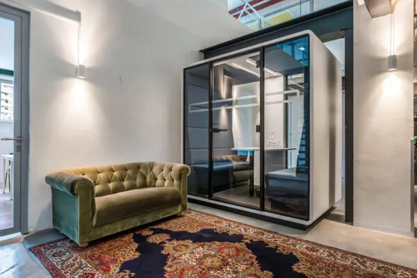 Moderne kantoorruimte met een glazen vergaderpod, een groenfluwelen chesterfieldbank en een klassiek tapijt.