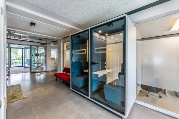 Moderne kantoorruimte met twee geluidsdichte belcellen, een rode bank en glazen wanden.