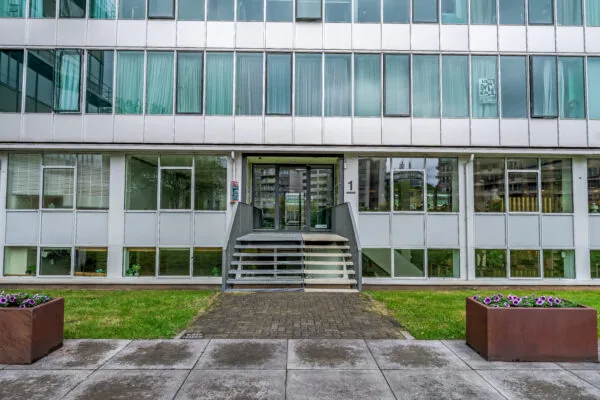 Vooraanzicht van een modern kantoorgebouw met glazen gevel en een centrale entree met trap en hellingbaan.
