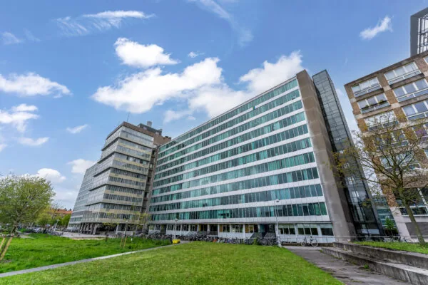 Modern kantoorgebouw met glazen gevel en omliggend groen grasveld onder een blauwe lucht.