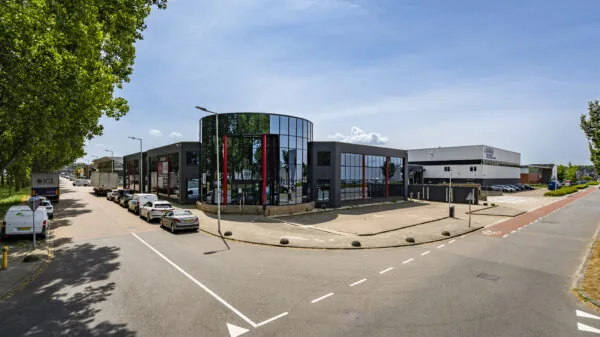 Modern bedrijfspand met glazen gevel en omliggende parkeerruimte aan een rustige industriële straat.