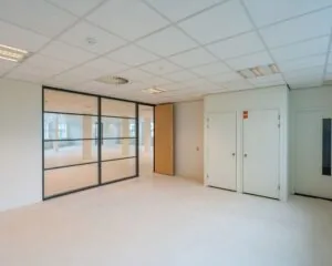 Lichte, lege kantoorruimte met glazen tussenwand en houten deur.