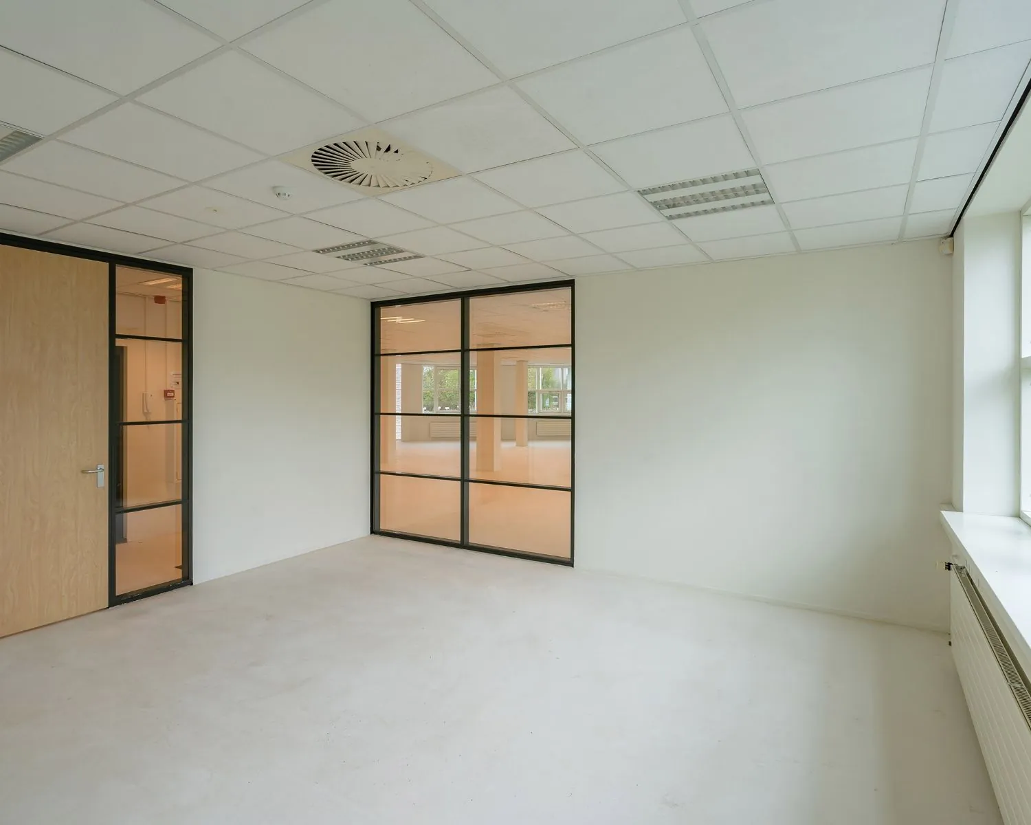 Licht en leeg kantoor met glazen tussenwand, houten deur en systeemplafond.