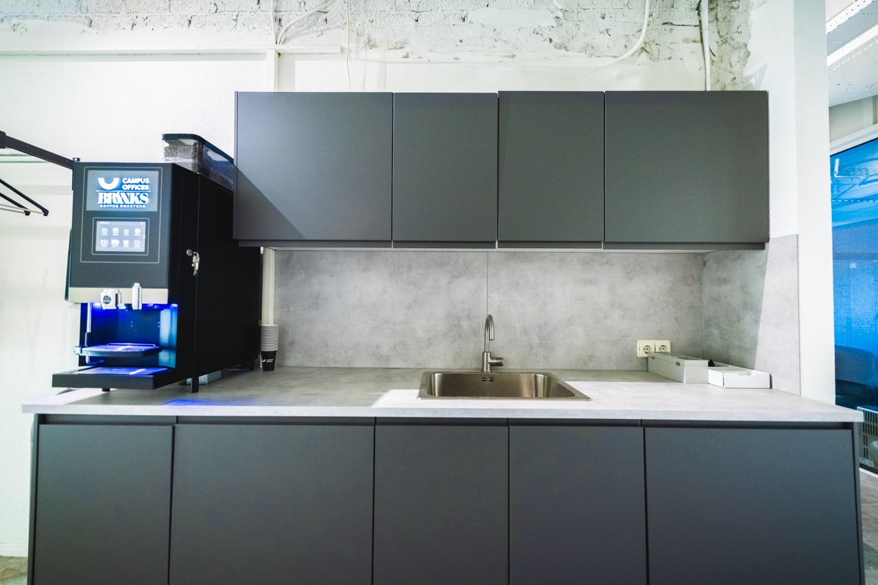 Moderne kantoorpantry met een koffieautomaat van Campus Offices BRUINS, een spoelbak en grijze keukenkasten.