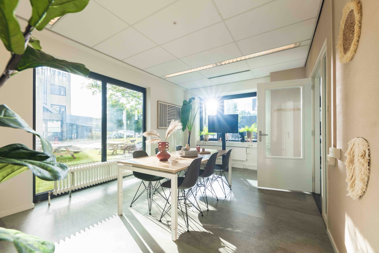 Licht en modern ingerichte vergaderruimte met grote ramen, een houten tafel en zwarte stoelen.