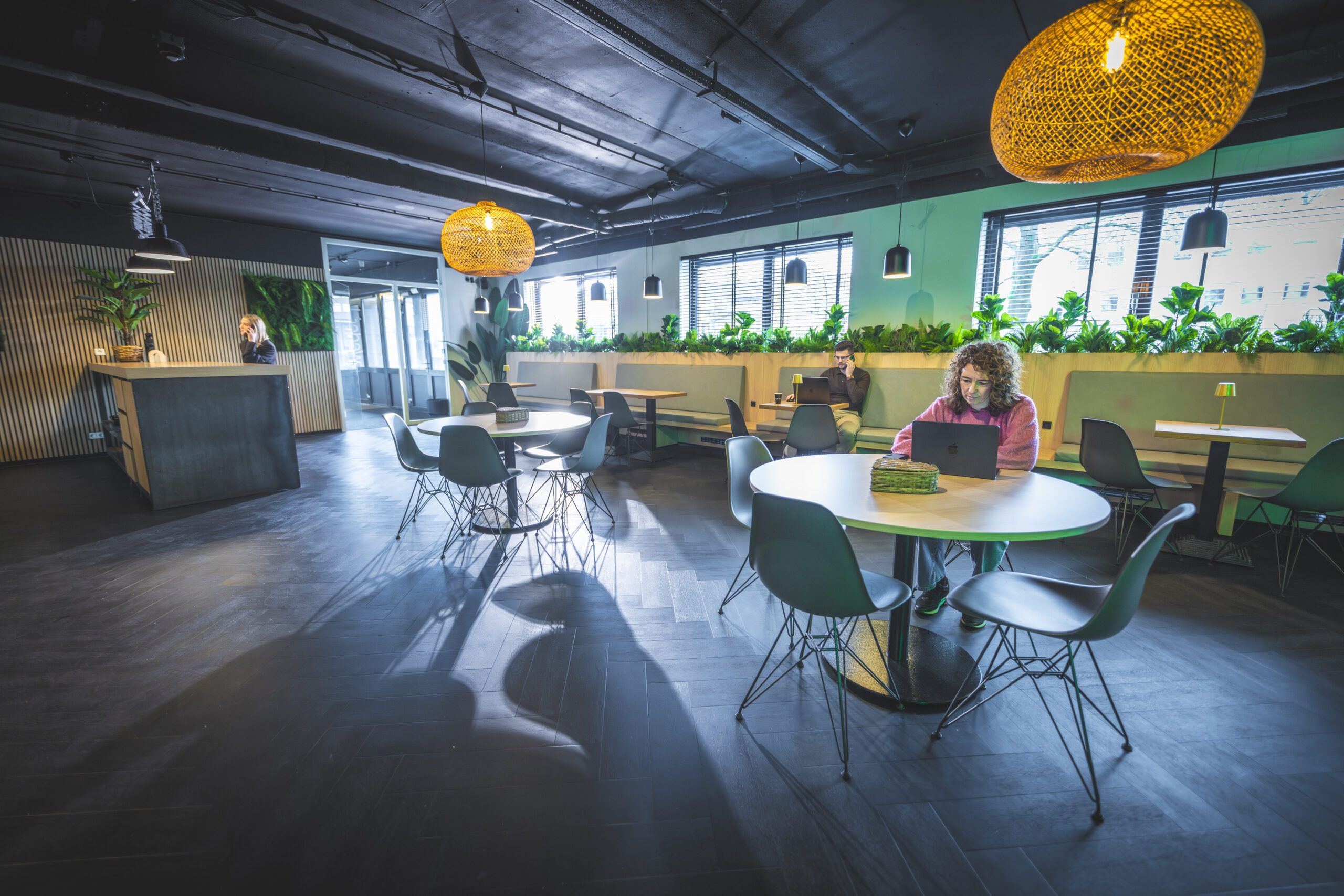 Moderne en sfeervolle lounge- en werkruimte met mensen die op laptops werken aan ronde en vierkante tafels.