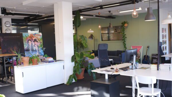 Moderne creatieve kantoorruimte met planten, bureaus, boekstapels en kleurrijke posters, waaronder één met de titel "DSCF6596".