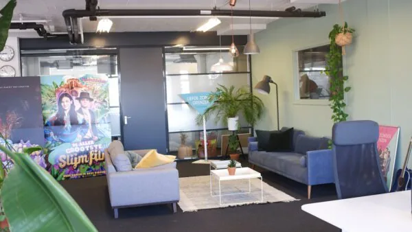 Moderne kantoorruimte met comfortabele zitbanken, kamerplanten en een kleurrijke filmposter van "De Allergrootste Slijmfilm".