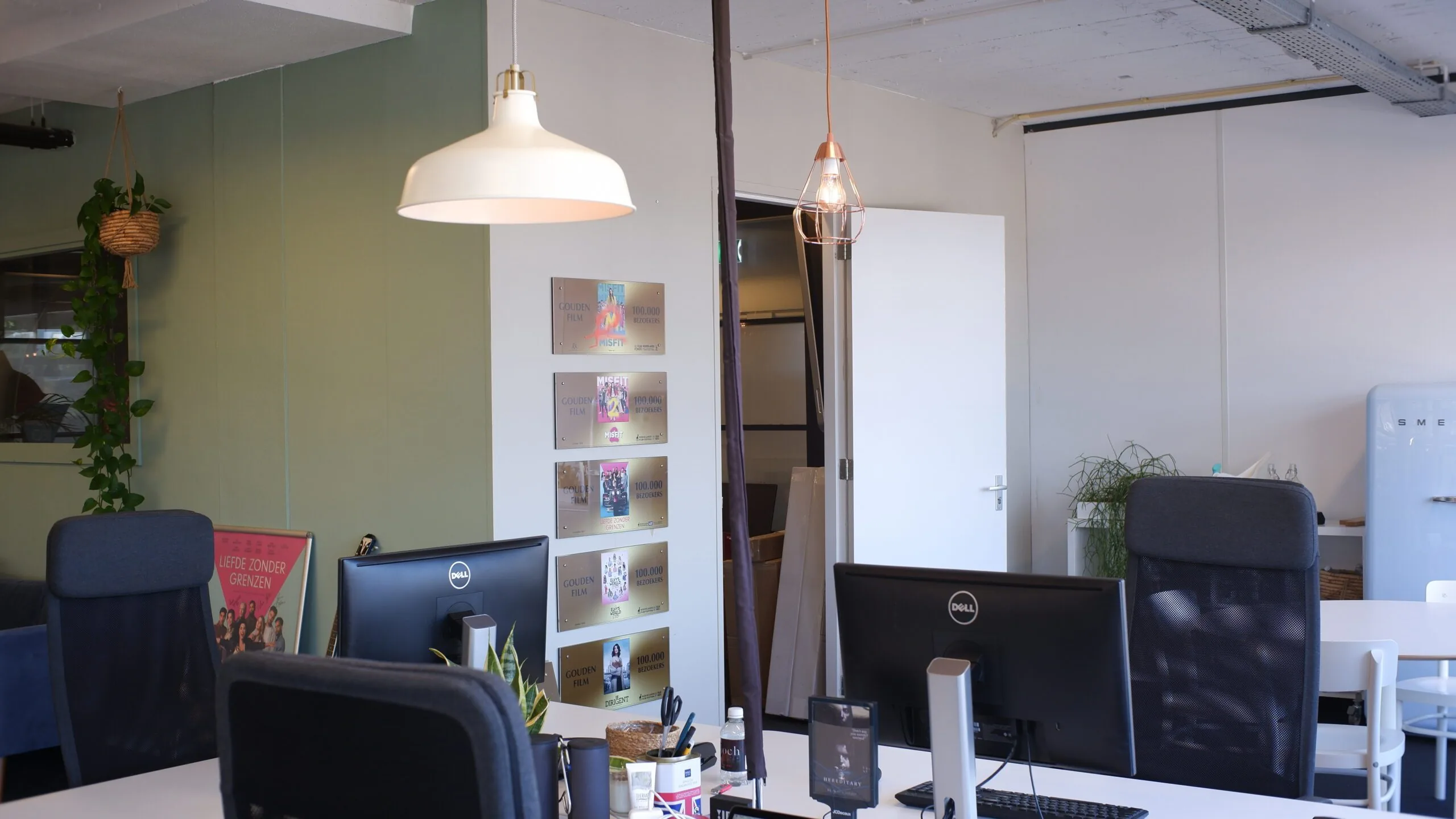 Modern kantoor met bureaus, computers, planten en filmprijzen aan de muur.