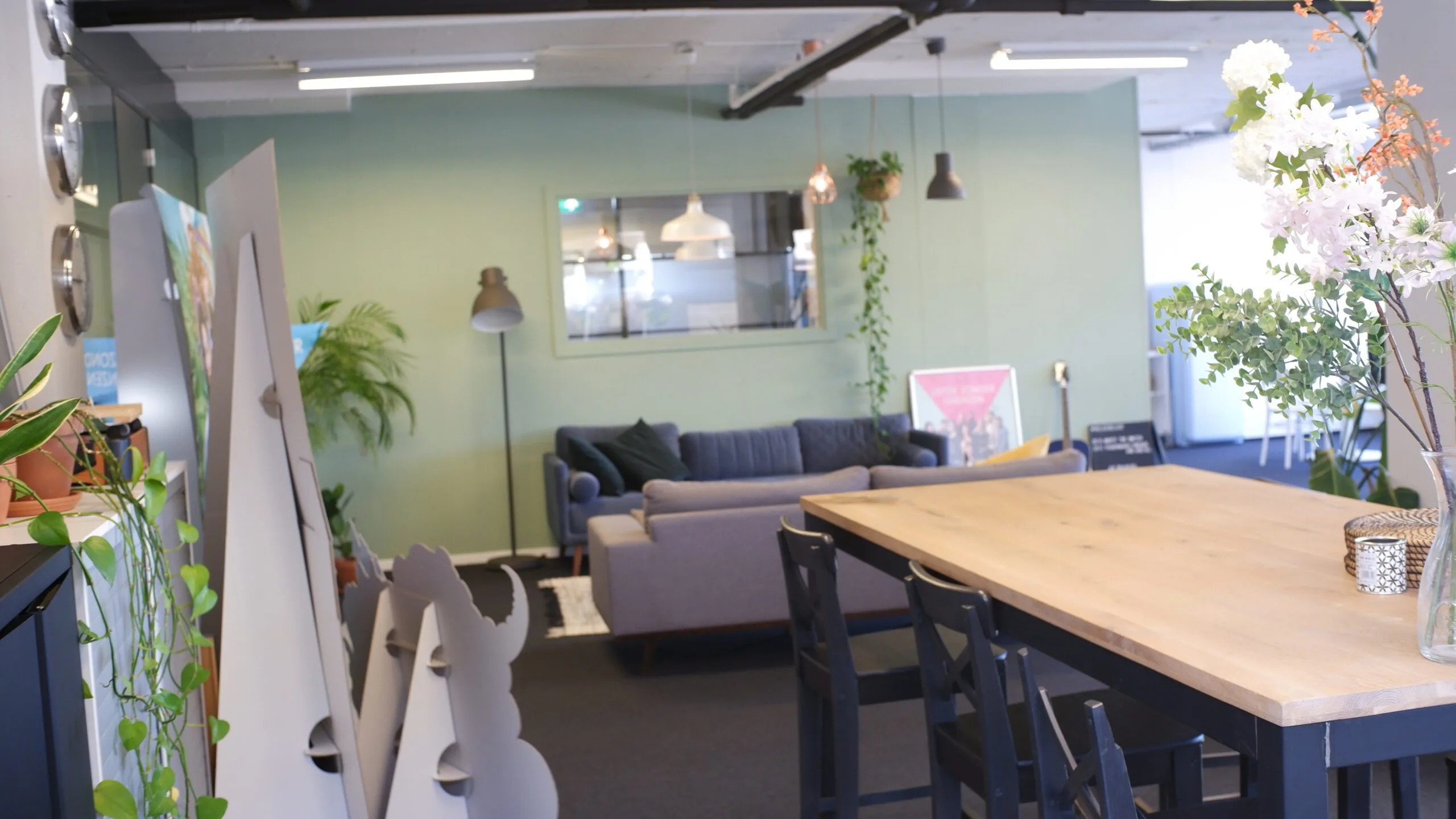 Moderne en sfeervolle loungehoek met banken, planten en een grote houten tafel in een kantoorruimte.