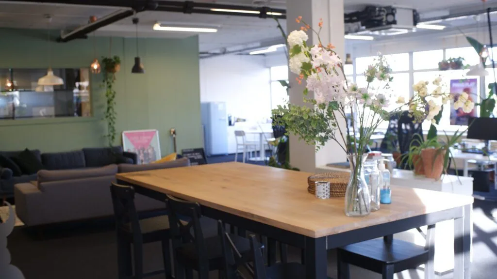 Een moderne kantoorruimte met een houten tafel, bloemen in een vaas en een groene accentmuur op de achtergrond.