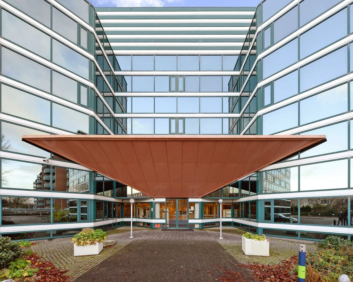 Ingang van een modern kantoorgebouw met glazen gevel en opvallende driehoekige luifel.