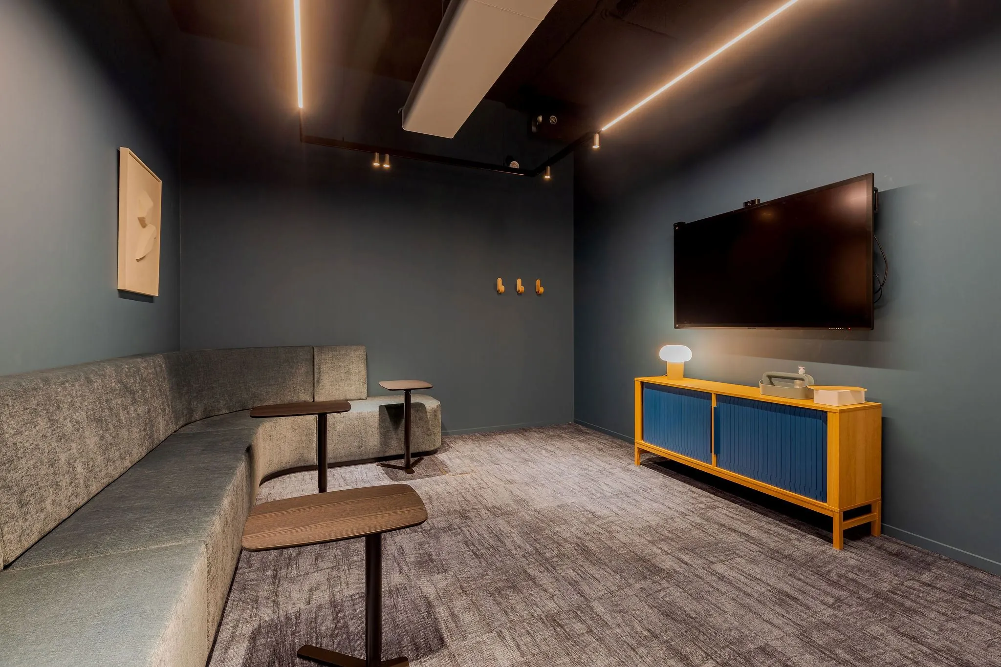 Moderne vergaderruimte aan de Daalsesingel 51 met een gebogen bank, losse bijzettafels, wandtelevisie en een houten dressoir met blauwe panelen.