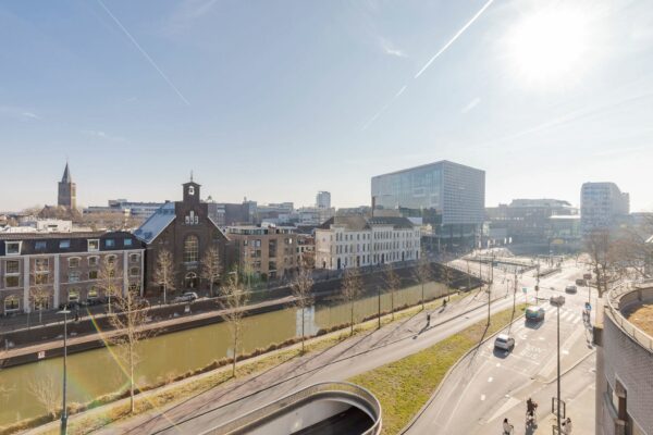 Zonnig stadsgezicht op de Daalsesingel in Utrecht met het kanaal, historische en moderne gebouwen, en fietsers en auto's op de weg.