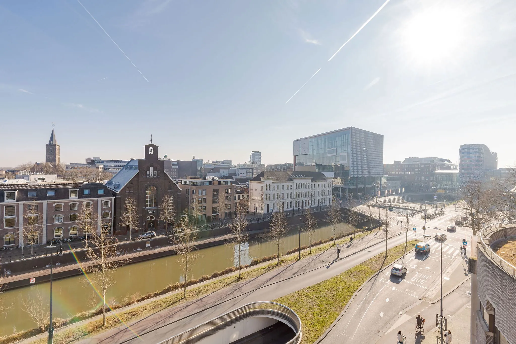 Zonnig stadsgezicht op de Daalsesingel in Utrecht met het kanaal, historische en moderne gebouwen, en fietsers en auto's op de weg.