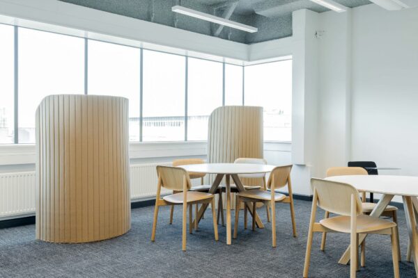 Moderne kantooruimte aan de Daalsesingel 51 met houten stoelen, ronde tafels en akoestische panelen bij grote ramen.