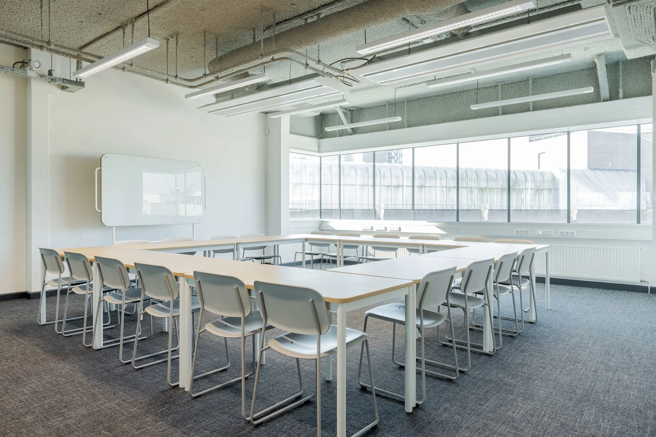 Licht en modern klaslokaal aan de Daalsesingel 51 met U-opstelling van tafels, grijze stoelen en groot raam.