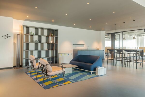 Moderne loungehoek in kantoorruimte aan de Daalsesingel 51 met designmeubilair, kleurrijk vloerkleed en open wandkast.