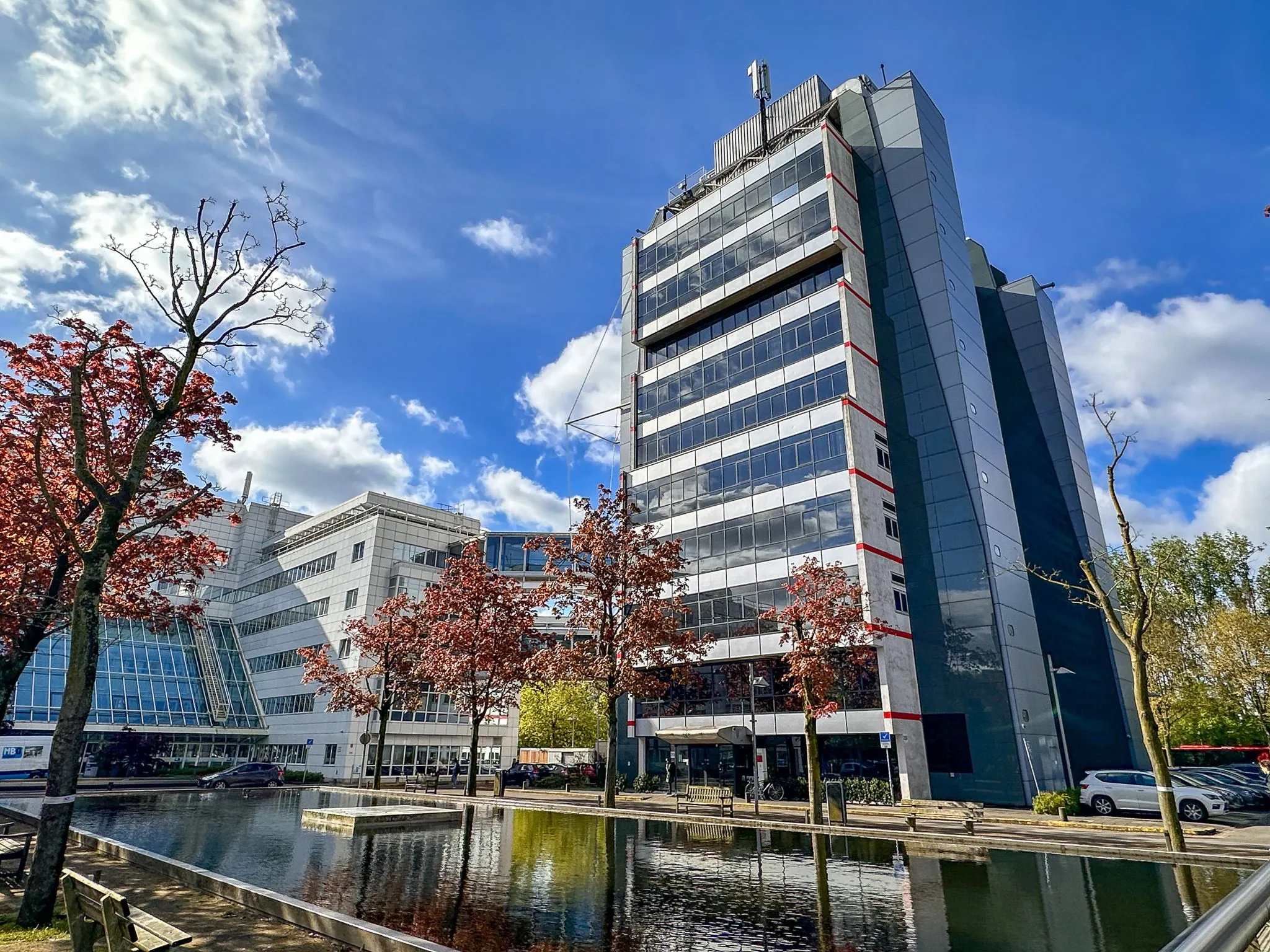 Kantoorgebouw aan de Daltonlaan 200 met moderne gevel, weerspiegeld in een vijver onder een blauwe lucht.