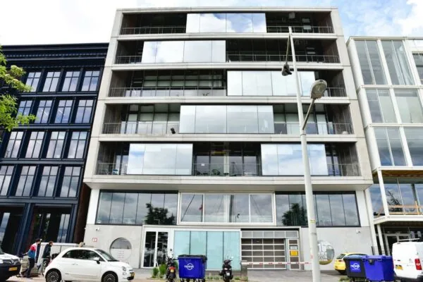 Vooraanzicht van het moderne kantoorgebouw aan de Danzigkade 16 met glazen gevel en geparkeerde voertuigen op straat.