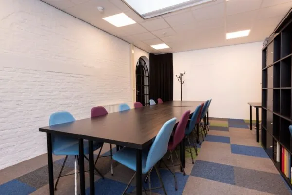 Vergaderruimte De Kaai Suiker met lange tafel, kleurrijke stoelen en moderne inrichting.