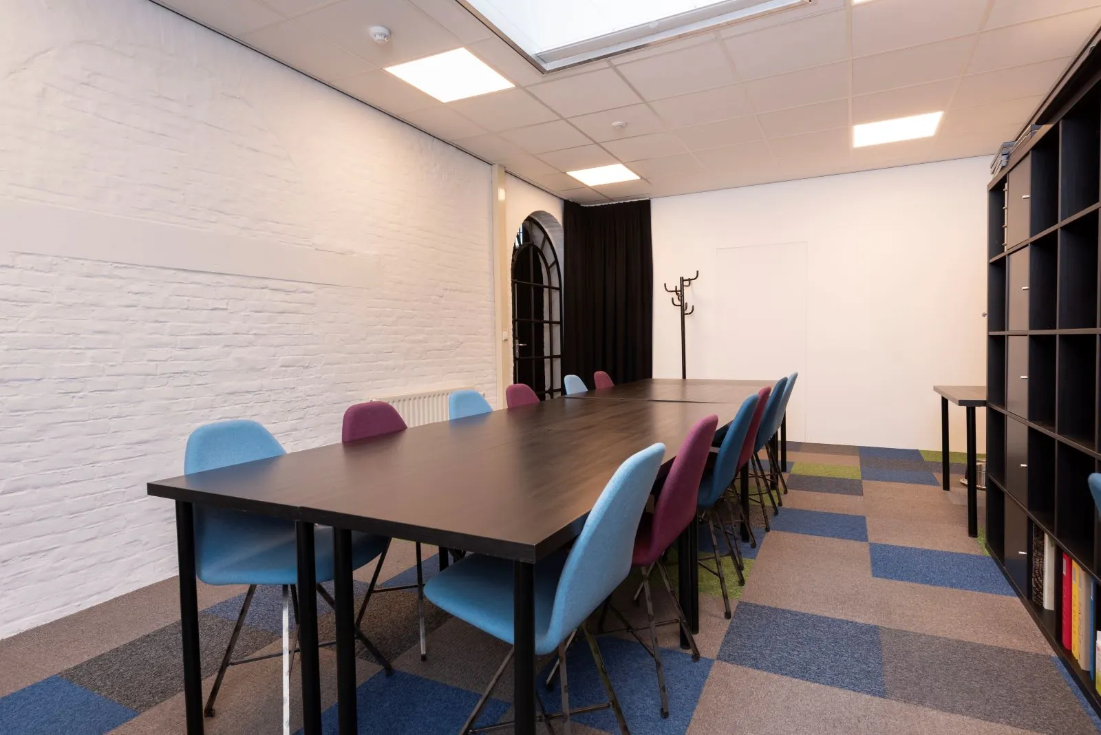 Vergaderruimte De Kaai Suiker met lange tafel, kleurrijke stoelen en moderne inrichting.