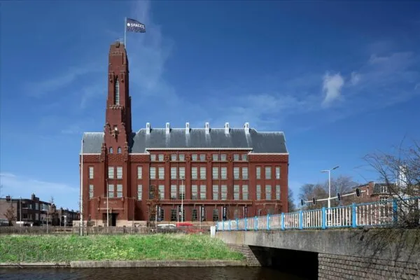 De Rode Olifant, een imposant rood bakstenen kantoorgebouw met toren aan het water in Den Haag, onder een heldere blauwe lucht.