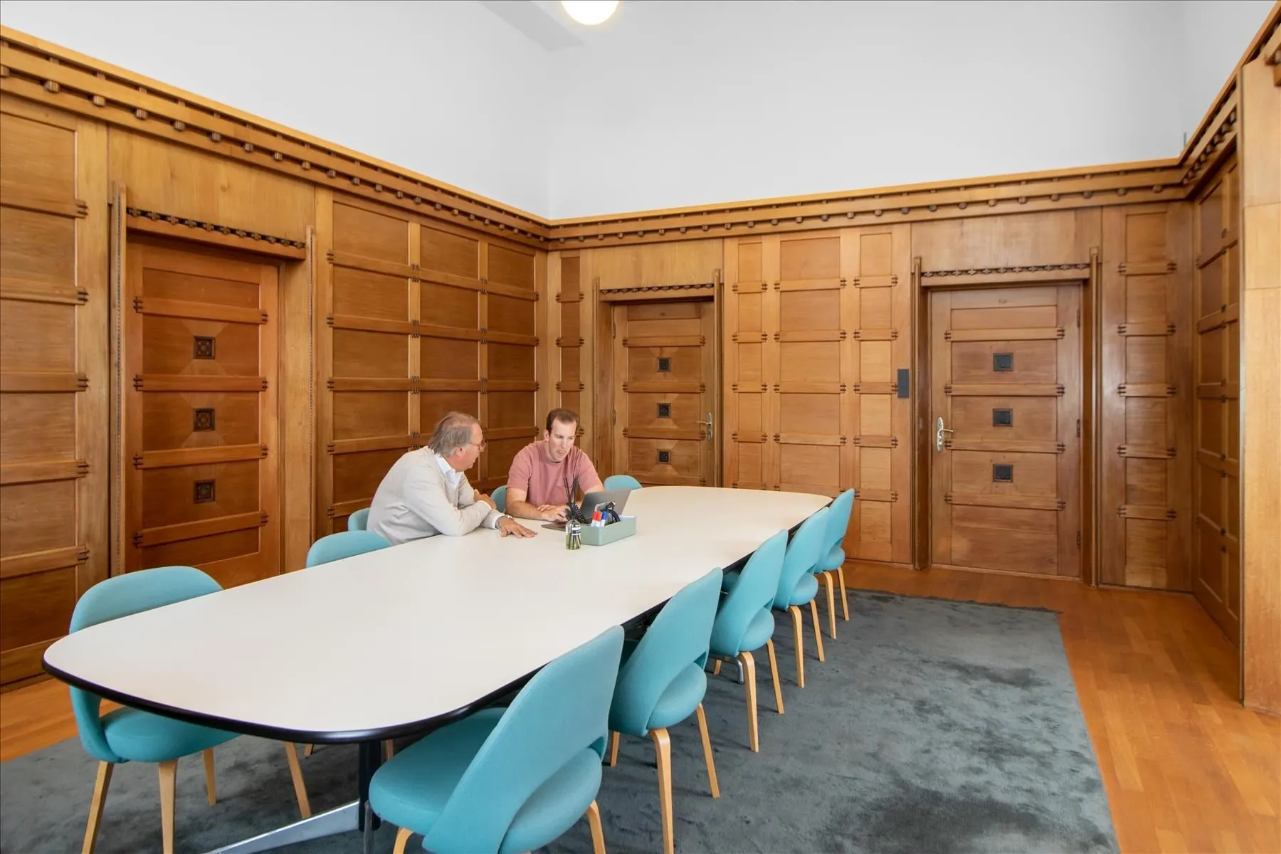 Twee mannen overleggen aan een lange vergadertafel in een houten vergaderruimte in De Rode Olifant.