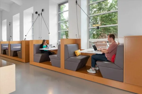 Twee mensen werken op laptops in moderne werkplekken met nisbanken bij De Rode Olifant.