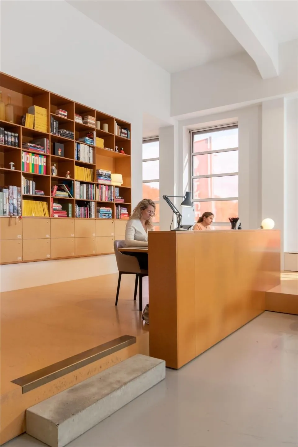 Twee vrouwen werken aan een oranje balie in een modern kantoorinterieur bij De Rode Olifant.