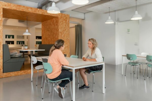 Twee vrouwen zitten tegenover elkaar aan een tafel in een moderne, lichte ruimte bij De Rode Olifant.