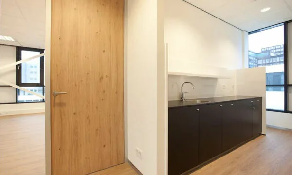 Moderne kantoorkeuken met donkerbruine kasten en houten deur in een ruimte aan de De Boelelaan 30.