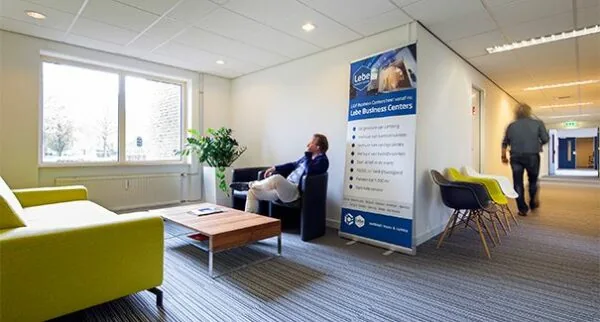 Wachtruimte in een kantoorgebouw aan de Dr. Nolenslaan met zitmeubilair, een banner van Lebe Business Centers en twee personen.