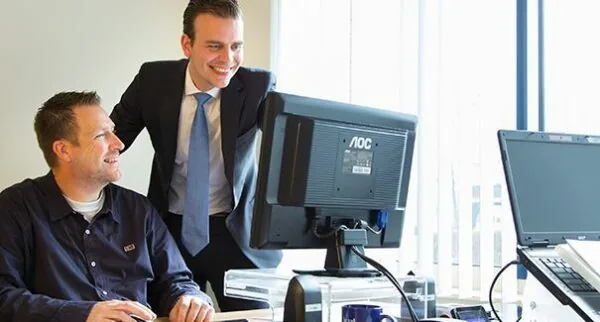 Twee mannen werken samen achter een bureau met computerschermen op een kantoor aan de Dr. Nolenslaan 157.