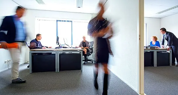 Kantoorruimte aan de Dr. Nolenslaan 157 met meerdere mensen aan het werk en anderen die door de gang lopen.