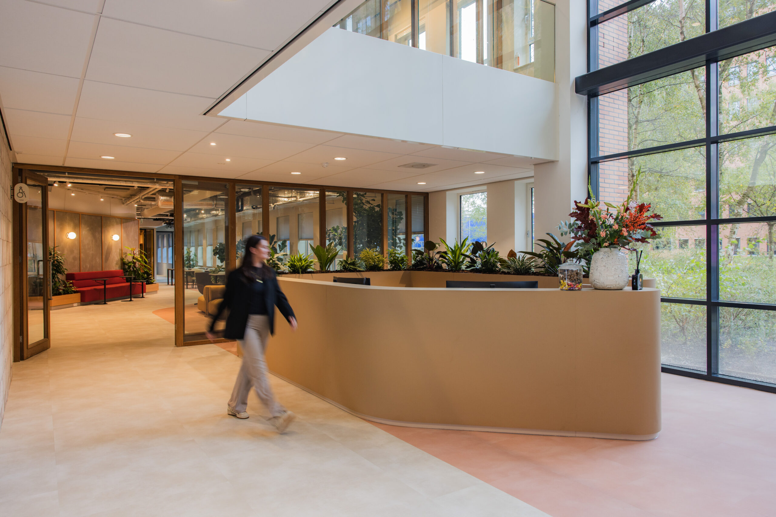 Modern reception area at Hullenberg with natural light, indoor plants, and a person walking past the desk.