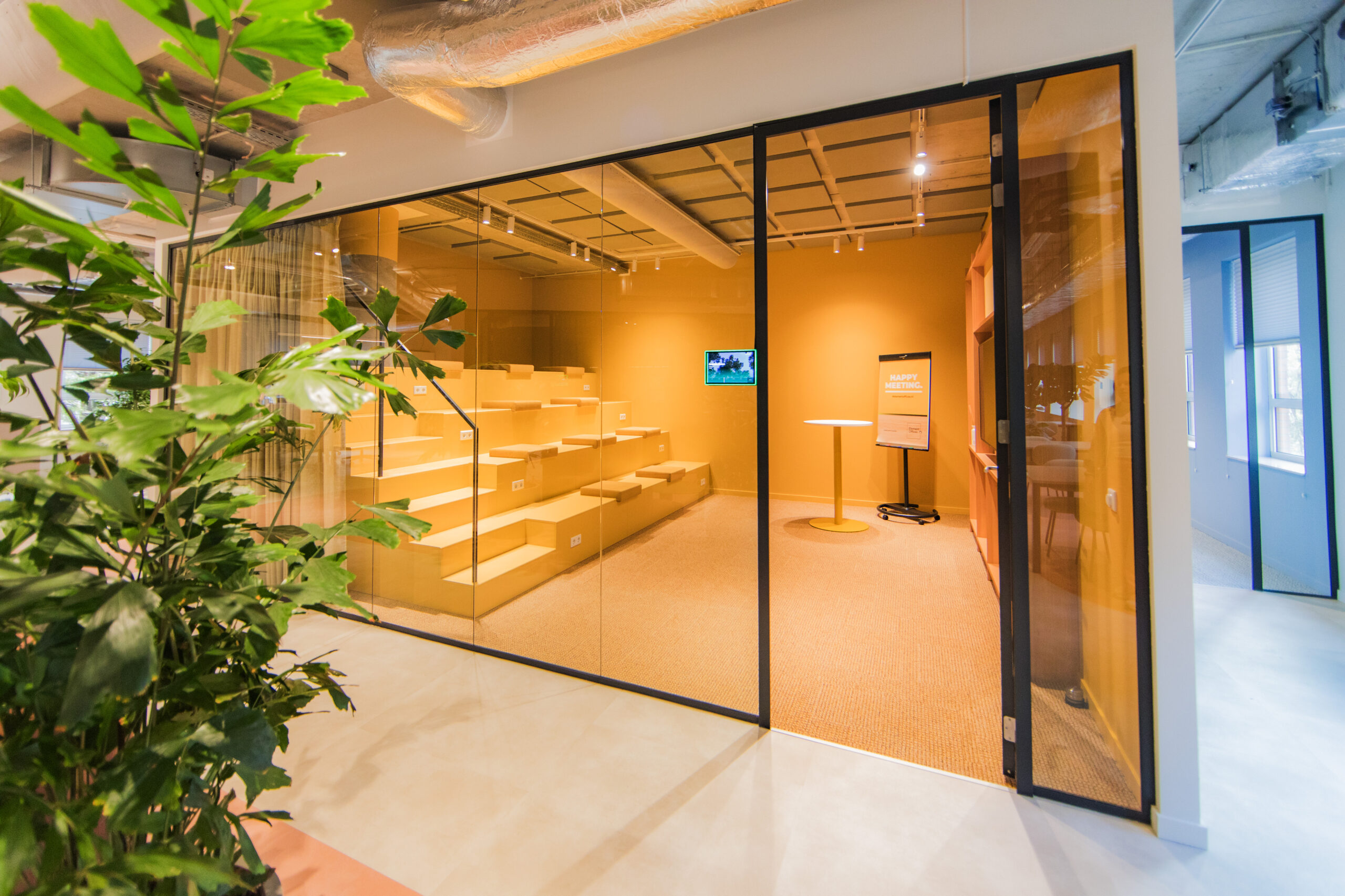 Modern yellow meeting space with tiered seating and glass walls at Hullenberg office.