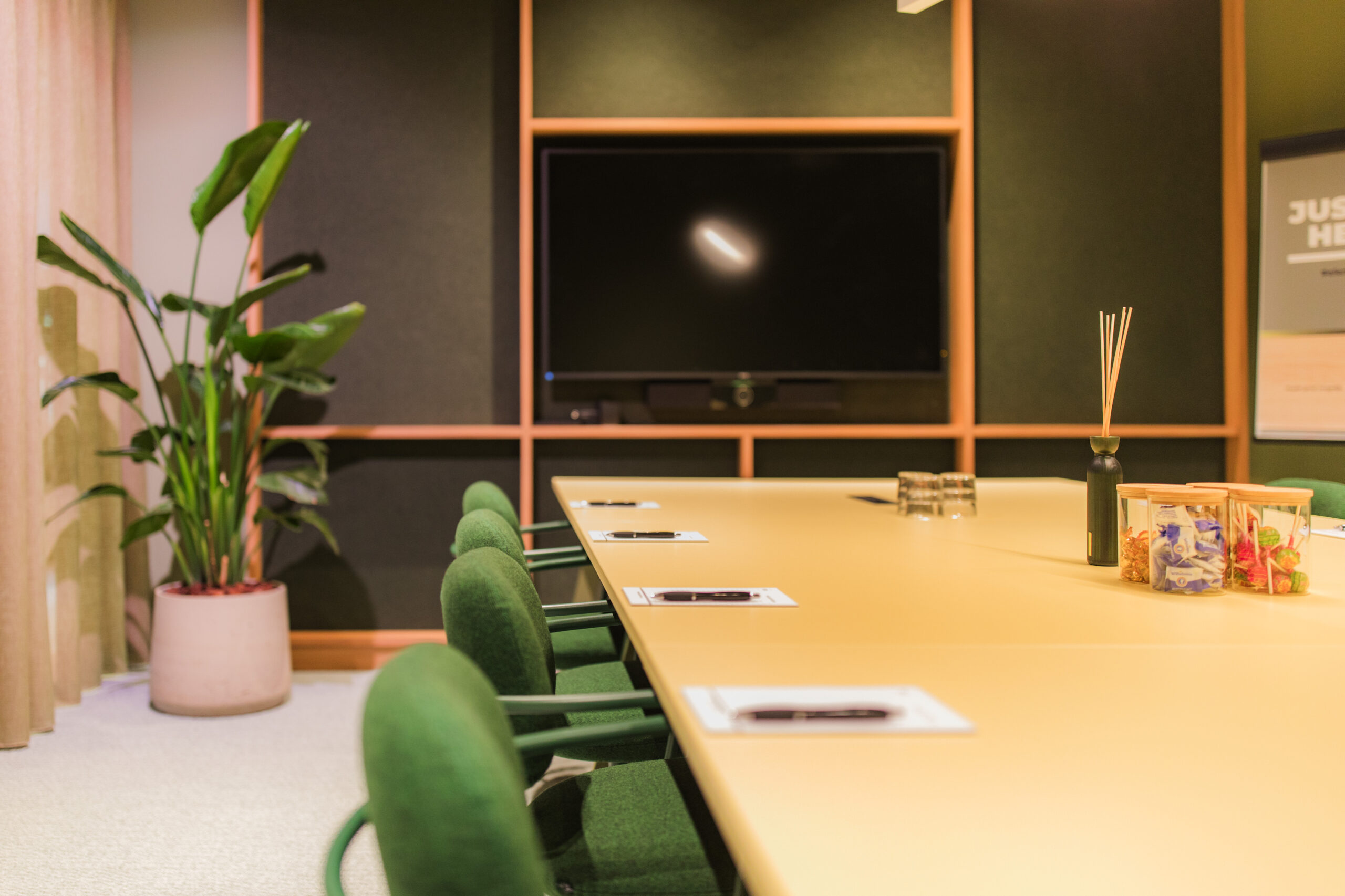 Modern conference room at Hullenberg with a large screen, green chairs, a beige table, and decorative items.