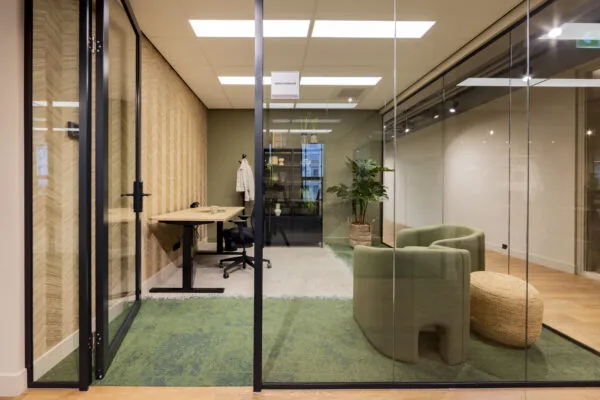 Moderne, glazen kantoorruimte in EO Diemen met een bureau, groene stoelen en planteninrichting.