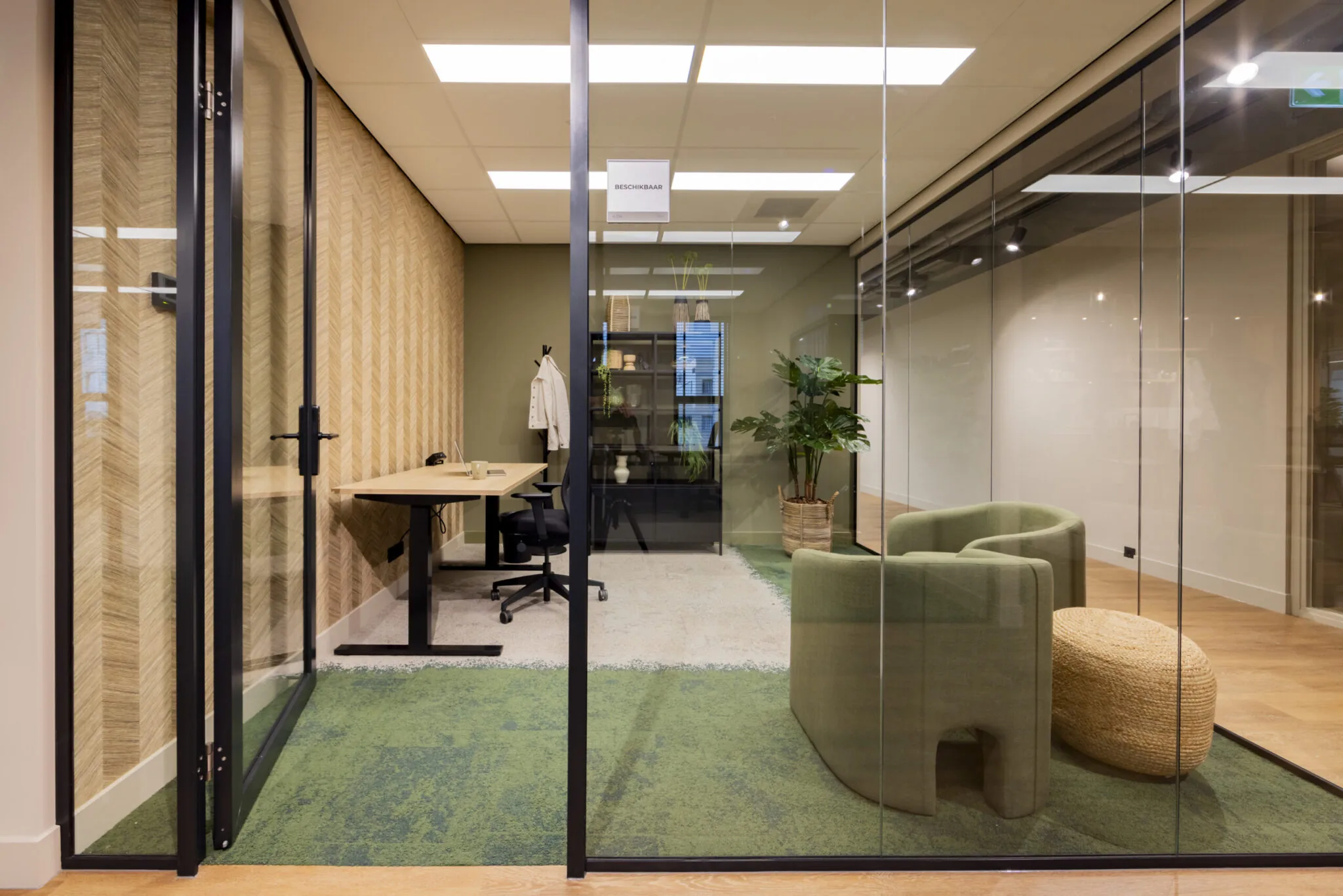 Moderne, glazen kantoorruimte in EO Diemen met een bureau, groene stoelen en planteninrichting.