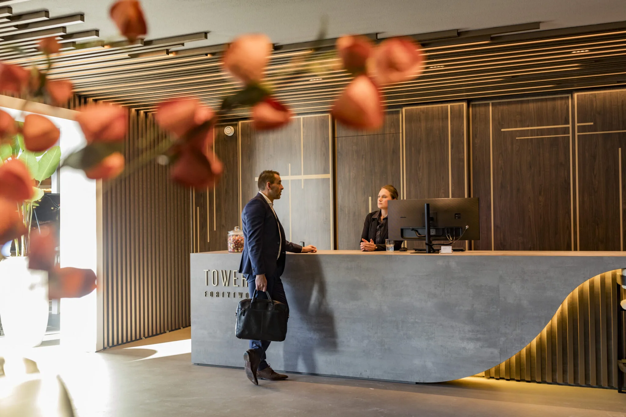 Een zakenman spreekt met een receptionist bij de balie van Tower FortyTwo in Diemen, met bloemen op de voorgrond.